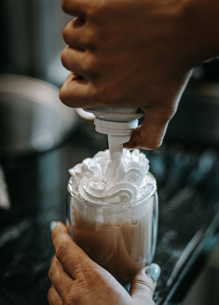 adding whipped cream to a coffee glass